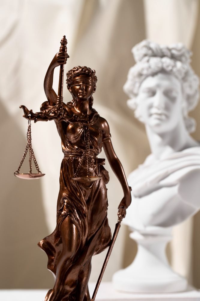 Estatua de bronce de la justicia junto a un busto clásico